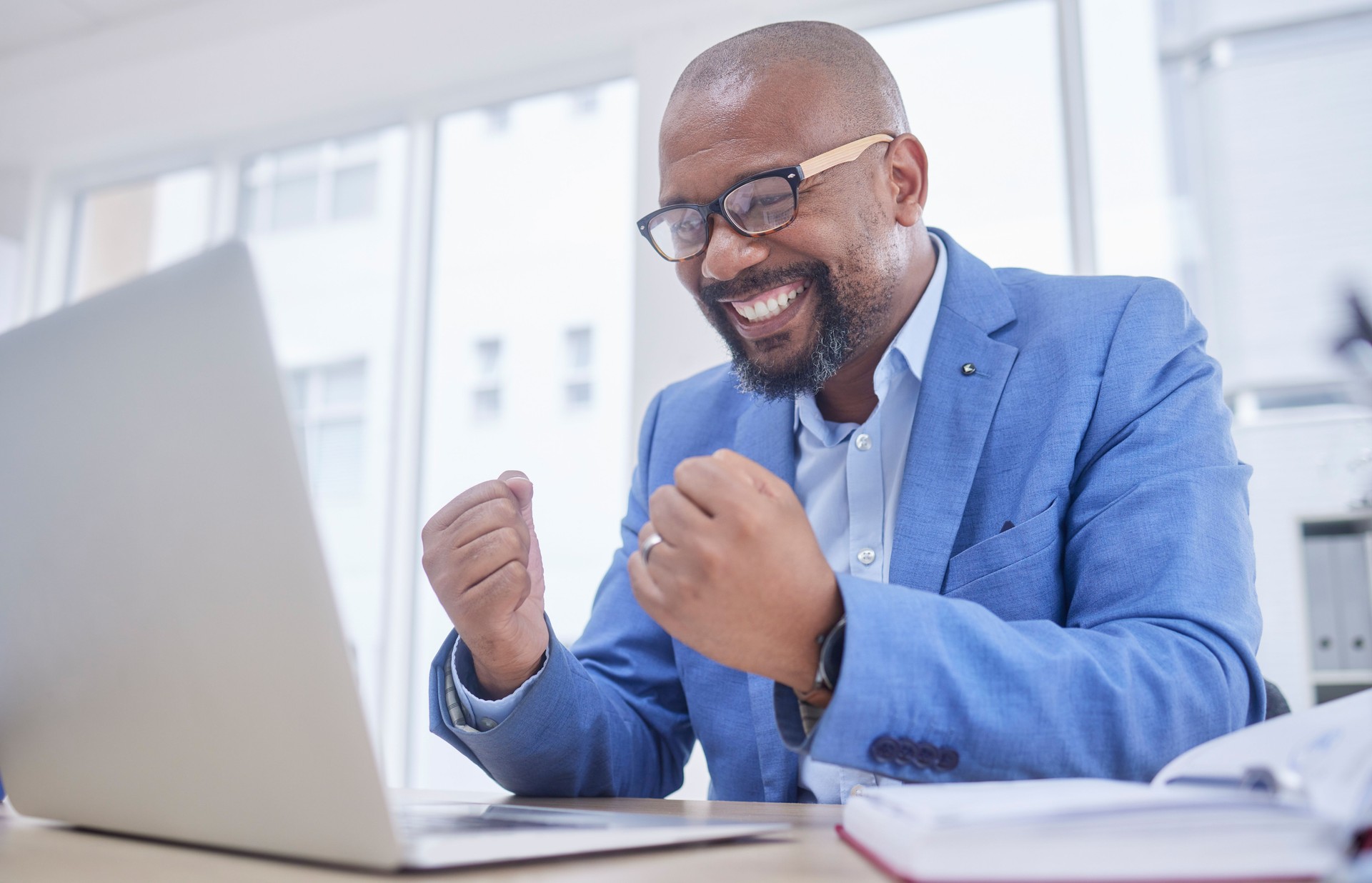 Black man, laptop and fist celebration in office for web design success, happiness or winner achievement. African businessman, celebrate and happy hands for online communication on digital device